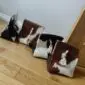 Four pyramid-shaped cowhide door stoppers in various brown, black, and white patterns on a wooden floor.
