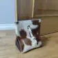 Square brown and white cowhide door stopper with a white leather handle on a wooden floor.