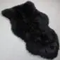 Irregularly shaped black sheepskin rug with thick, curly wool texture.