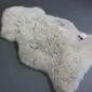 Natural oyster-coloured curly sheepskin rug with a thick, textured wool pile and organic shape.
