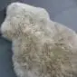 Small stone grey sheepskin rug with thick, natural wool pile in an organic shape.