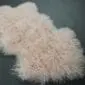 Blush pink Mongolian lambskin rug with long, curly wool fibres and an irregular natural shape.