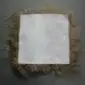 Underside of a square taupe Icelandic sheepskin pad showing the white leather backing and long wool fringe.