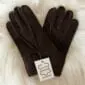 A pair of dark brown sheepskin gloves with a white product tag, displayed on a cream textured surface.