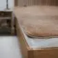 Brown camel and merino wool mattress topper with rounded corners and piped edges on a bed.