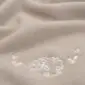 Close-up of a beige merino wool blanket featuring white embroidered sheep and heart patterns.