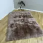 Rectangular sheepskin rug with thick, long-pile brown wool on a wooden floor.