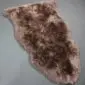 Irregularly shaped sheepskin rug with long, textured wool in mottled shades of brown and cream.