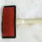 Sheepskin-Rug-Brush-02-1.jpg Sheepskin rug brush with a light wooden handle and a rectangular red head featuring metal bristles.