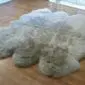 Large, multi-pelt sheepskin rug in vole grey with a thick, textured wool pile and natural scalloped edges.