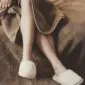 Beige wool slippers with a textured finish worn on feet.