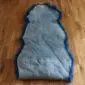 Underside of a navy blue double sheepskin rug showing the natural light grey suede backing.