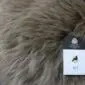 SHEEPSKIN RUG NZS-Taupe (1) Close-up of a taupe sheepskin rug with long, thick wool fibres and a product tag.