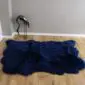 Large navy blue four skin sheepskin rug with a natural wavy edge on a wooden floor.