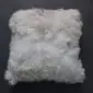Square white Tibetan sheepskin cushion with long, curly wool texture .
