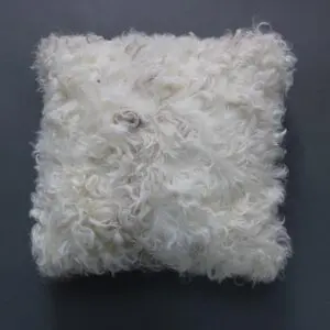 Square white Tibetan sheepskin cushion with long, curly wool texture . detail view