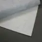 A thin, white rectangular anti-slip rug underlay positioned beneath a grey fabric rug on a dark floor.