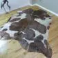 Natural brown and white cowhide rug with rose gold metallic splatters and an irregular shape.