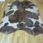 Natural shaped cowhide rug with brown and white patches and rose gold metallic speckles.