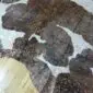 Close-up of a brown and white cowhide rug with metallic rose gold splatters across the surface.