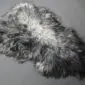 Natural grey curly sheepskin rug with variegated charcoal and silver tones and a textured, woolly finish.