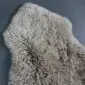 Beige curly sheepskin rug with a natural pelt shape and thick, textured wool.