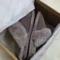 Mink-coloured sheepskin slippers with fluffy collars inside a cardboard box with white tissue paper.