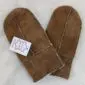 A pair of brown suede children's mittens with exposed cream sheepskin wool seams and a white product tag.