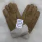 A pair of tan suede sheepskin gloves with visible cream wool lining and a white product tag.