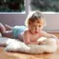 BabycareSoft-1a_900x A young child lying on a cream-coloured, thick-pile washable lambskin rug on a wooden floor.