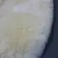 Close-up of a cream sheepskin stroller liner showing the thick, soft wool texture and rounded edge.