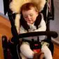 A sleeping child in a black pushchair lined with a cream sheepskin stroller liner.