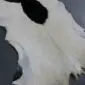 Natural goatskin rug with white and cream fur featuring a large black patch and irregular edges.