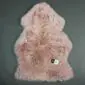 A dusty pink sheepskin rug with a natural pelt shape and thick, textured wool pile.