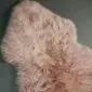 Irregularly shaped dusty pink sheepskin rug with thick, long wool fibres.