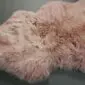 Irregularly shaped dusty pink sheepskin rug with long, thick wool pile.