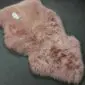 A dusty pink sheepskin rug with a thick, textured wool pile and natural organic shape.