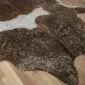 Close-up of a brown and white cowhide rug with metallic gold speckles on a wooden floor.