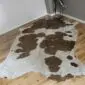 Natural shaped cowhide rug with brown and white patches and gold metallic splatters on a wooden floor.