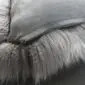 Close-up of a grey sheepskin cushion showing long, soft wool fibres and a smooth fabric reverse with a zip.