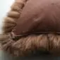 Close-up of a natural brown sheepskin cushion with a suede reverse and long wool trim.