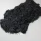 Black Tibetan lambskin rug with long, curly wool fibres on a light grey background.