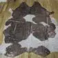 Natural brown and white cowhide rug with rose gold metallic splatters on a wooden floor.