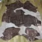 Natural brown and white cowhide rug with metallic rose gold splatters and an irregular shape.