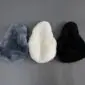Three sheepskin bicycle seat covers in grey, white, and black arranged in a row .