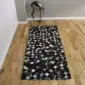 Rectangular patchwork cowhide rug featuring a grid of black and grey squares on a wooden floor. detail view