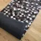 Patchwork cowhide rug featuring black, grey, and white squares with a dark textured backing.