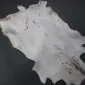 Natural goatskin rug with light grey fur, dark spots, and a brown stripe along the spine.