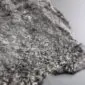 Close-up of a natural grey curly sheepskin rug showing dense, textured wool curls.