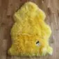 A bright yellow sheepskin rug with a thick, fluffy texture and natural pelt shape.